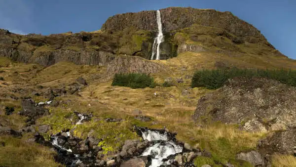 A thin, tall waterfall trickles down the terrai all the way to the photographer